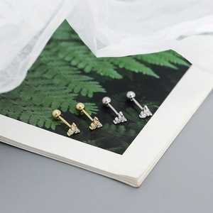 Detailed view of gold and silver S925 sterling silver clover stud earrings on leaf print