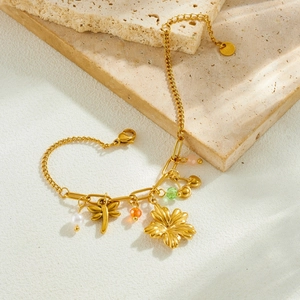Pastel gold stainless steel charm bracelet with dragonfly and flower on stone surface