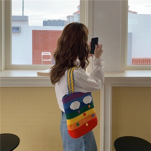 Detail of handmade rainbow knit bag with white 3D cloud patterns and colorful pom-poms