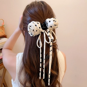 Detail of a beige polka dot hair bow with rose ruffles and long flowing ribbons