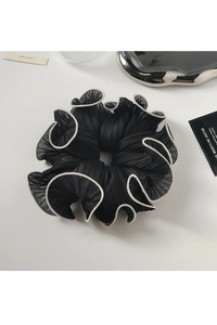 Detail of a large black pleated hair scrunchie with white piping on a minimalist tray