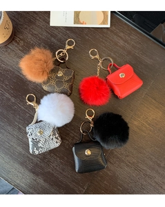Mini handbag keychains with plush fur balls and gold hardware on dark wood