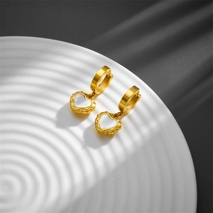 Golden heart earrings with mother of pearl inlay shown on a white textured plate