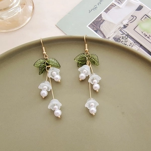 Detail of pink lily of the valley earrings with green leaves and pearls on ceramic edge