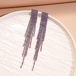 Close-up of long purple rhinestone tassel earrings on a textured white ceramic plate
