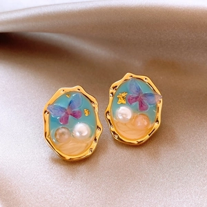Detail of French vintage earrings with gold edges, blue resin sky, and purple butterfly