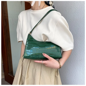 Detailed view of dark green crocodile pattern shoulder bag on model with soft lighting