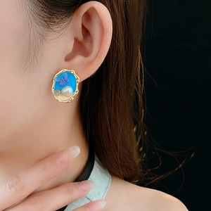 Dettaglio di orecchini vintage dorati con smalto blu, perle e farfalla viola su modella
