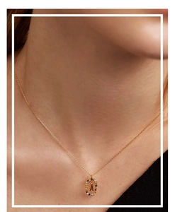 Macro detail of a gold letter A necklace with vibrant colored crystal gemstones on neck
