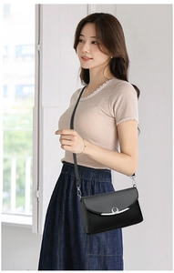 Detail of a black leather crossbody bag with silver ring clasp shown on a model