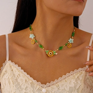 Detail of beaded necklace featuring enamel sunflower pendant and light blue resin flowers