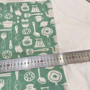 Close-up of green cotton linen pillowcase showing white hand-drawn kitchen pattern and scale