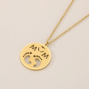 Macro detail of gold MOM necklace pendant with heart shape and baby footprints engraving