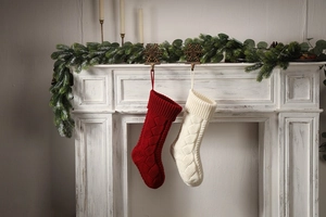 Knitted Christmas stockings in red and cream with cable patterns hanging on a fireplace
