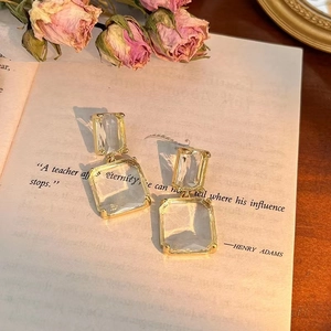 Elegant gold rectangular earrings with clear geometric crystals on vintage book background