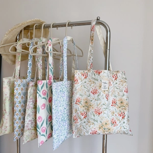 Détail de plusieurs sacs fourre-tout en toile à motifs floraux suspendus sur un portant