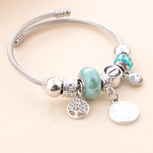 Macro detail of silver-plated twist bangle with light green beads and tree of life charms