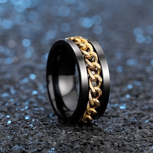 Close-up of matte black spinning ring with gold Cuban chain inlay on a textured surface