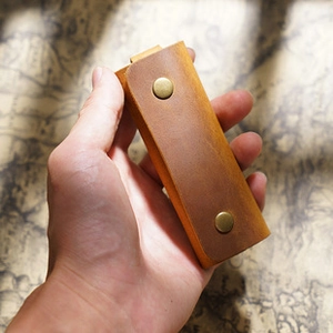 Handheld view of a vintage brown crazy horse leather mini measuring tape with brass snaps
