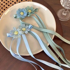 Blue daisy flower hair clips with long ribbons displayed on a white ceramic plate