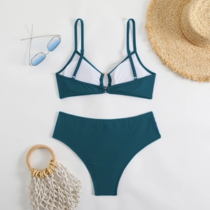 Flat lay of a dark teal bikini set with sunglasses and straw hat on white background