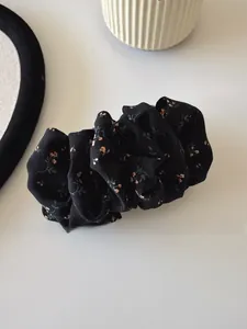 Macro shot of black floral pattern scrunchie with pink flowers on a white surface