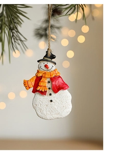 Close-up of a resin snowman ornament with red scarf and hat hanging on a Christmas tree
