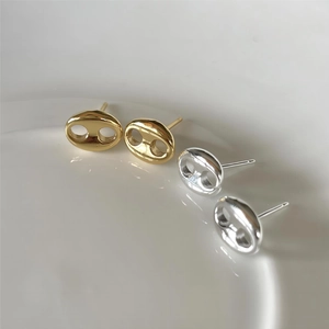 Polished silver and gold pig nose earrings set against white ceramic detail