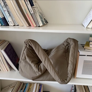Detail of a khaki puffer tote bag with a soft quilted texture on a white bookshelf