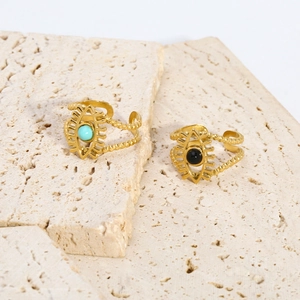 Detail of gold evil eye rings featuring turquoise and black stones on stone surface