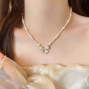 Close-up of pearl necklace with a sparkling zircon bow pendant on female model