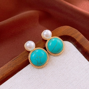 Close-up of vintage gold rimmed turquoise stud earrings with pearls on burlap
