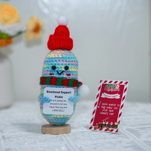 Close-up of handmade crochet emotional support pickle with festive Santa hat and cards