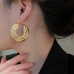 Detail of gold chunky hoop earrings with embossed diamond quilted texture worn by model