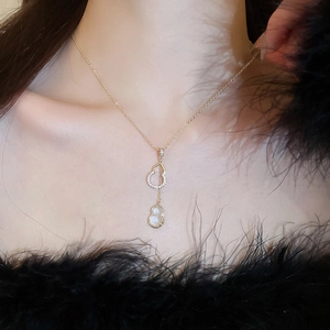 Détail du collier double gourde dorée avec cristaux sur un modèle avec plumes noires