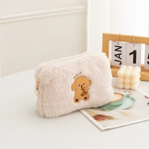 Detailed close-up of pink plush makeup bag with poodle embroidery and pearl zipper pull