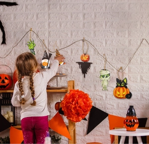 Girl decorating a white wall with festive Halloween wooden ghost and pumpkin pendants