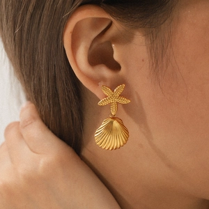 Golden stainless steel starfish and shell drop earrings worn as a closeup fashion set