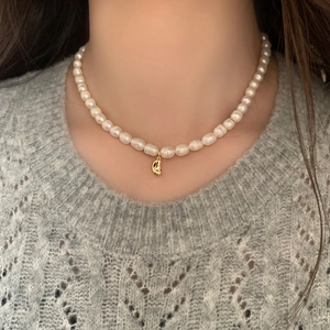 Close-up of natural freshwater pearl necklace with a gold bean pendant worn by model