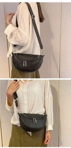 Detail of black pebbled leather crescent bag with silver zippers on an adjustable strap