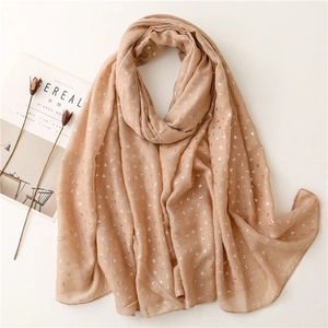 Detailed view of beige scarf with gold polka dots styled with dried flowers and a magazine