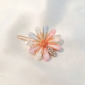 Detailed view of daisy hair clip with gradient petals and rhinestones on silk background