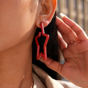 Close-up of a model wearing high-shine red acrylic star earrings with steel pins