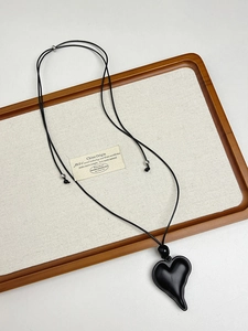 Close-up of black resin heart pendant necklace with adjustable woven rope on wooden tray