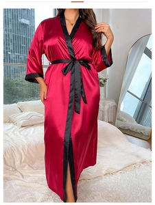 Detail of red satin robe with black trim and belt in a cozy bedroom setting