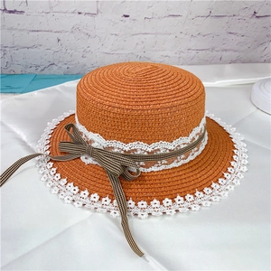 Close-up of orange straw hat featuring white lace trim and a black and white checkered bow