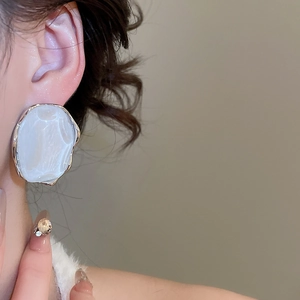 Detailed close-up of French resin geometric white earrings with gold plating on ear