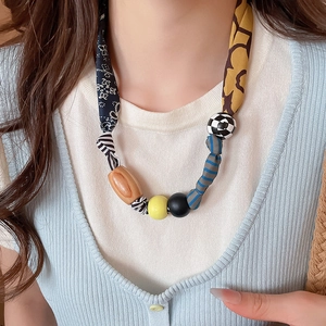 Détail de perles en tissu imprimé et d'éléments en bois sur un collier avec pendentif cœur