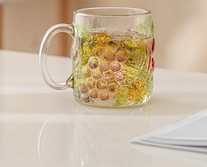 Close-up of hand-painted grape and flower embossed patterns on transparent glass mug