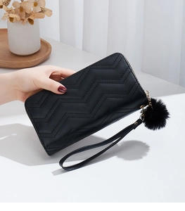 Detail of black wave quilted wallet featuring a zip closure and a plush ball charm